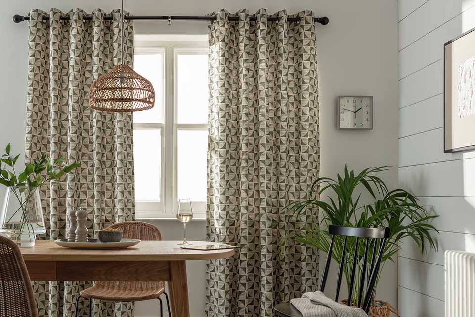 Green Habitat Cabin Geo Print Lined Eyelet curtains drawn over a window with plants on either side of it.
