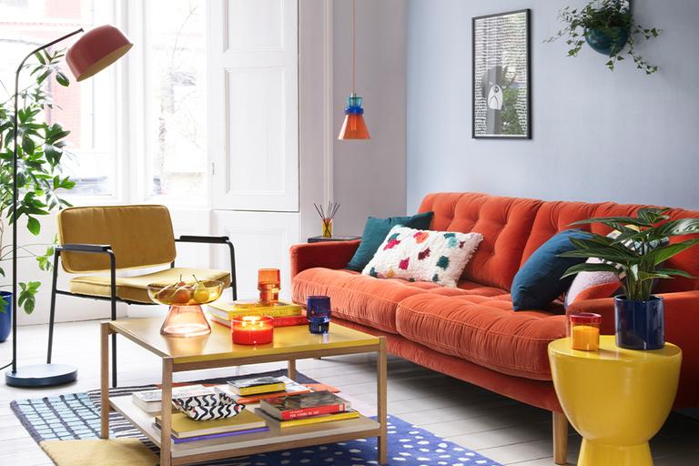 A living room bright multi-coloured furniture and home accessories including a tangerine orange sofa, yellow coloured coffee table, side table and an armchair.