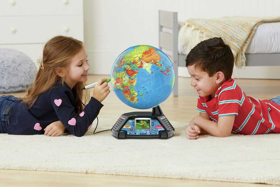 A boy and a girl playing wtih LeapFrog Magic Adventures Globe lying down on a rug.