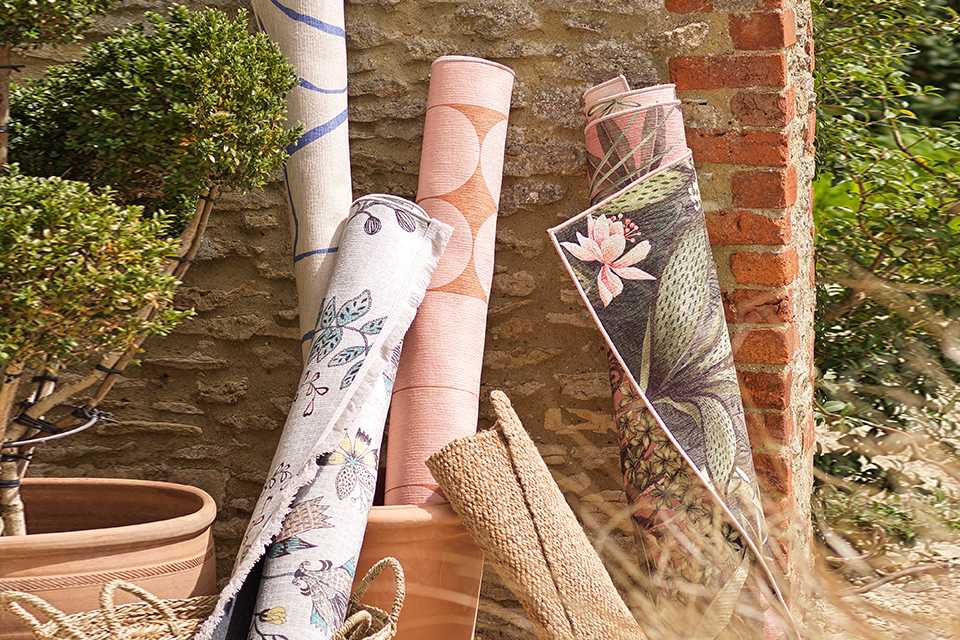 Four varieties of rugs rolled and stacked near a wall in a garden.