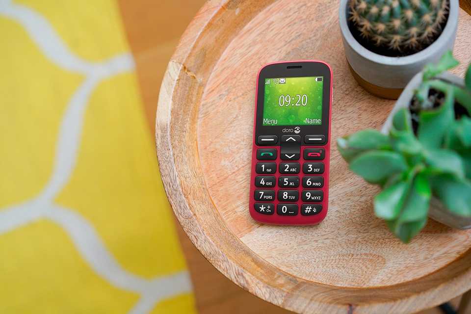 A Doro 1380 feature phone in red placed on a table top next to two potted plants.
