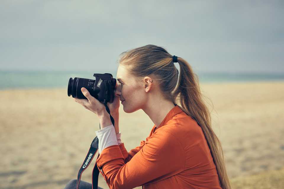 A woman taking photographs with a Canon DSLR camera at the beach.