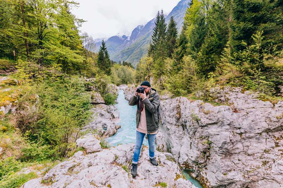 A man taking photographs with a Canon DSLR camera against a mountain backdrop.