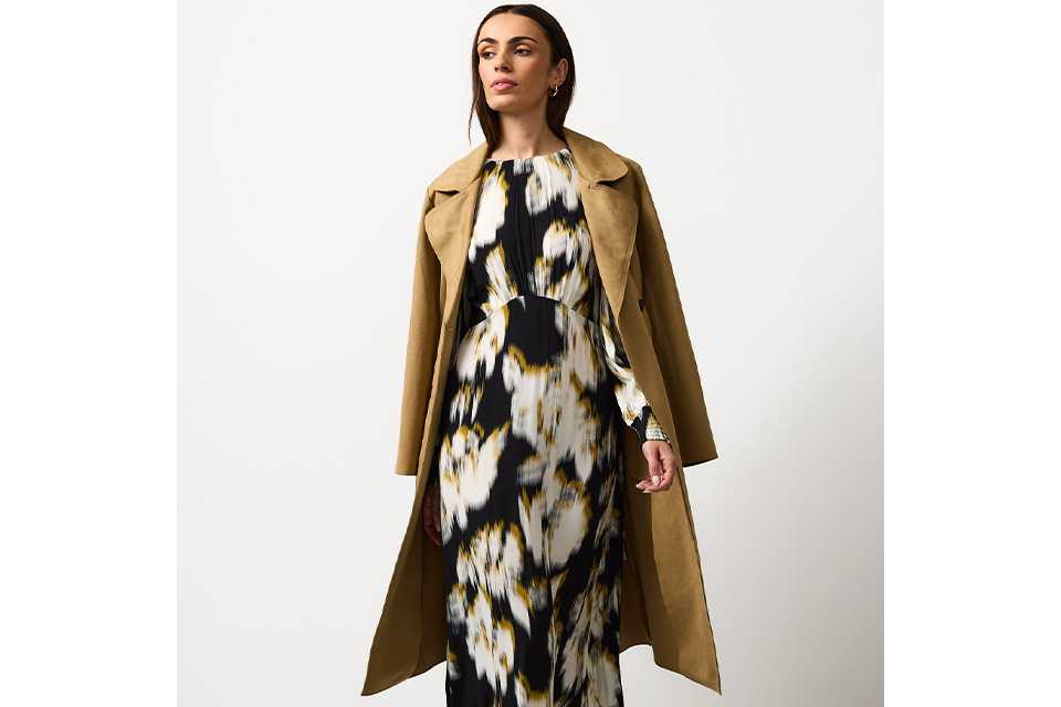 Black and cream abstract floral midi dress styled with a camel trench coat and neutral pointed heels on a white background.