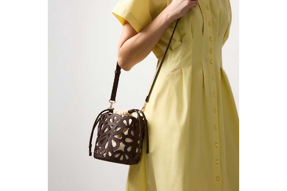 Light yellow short‑sleeve button‑front midi dress styled with a black cut‑out bucket bag and crossbody strap on a neutral studio background.