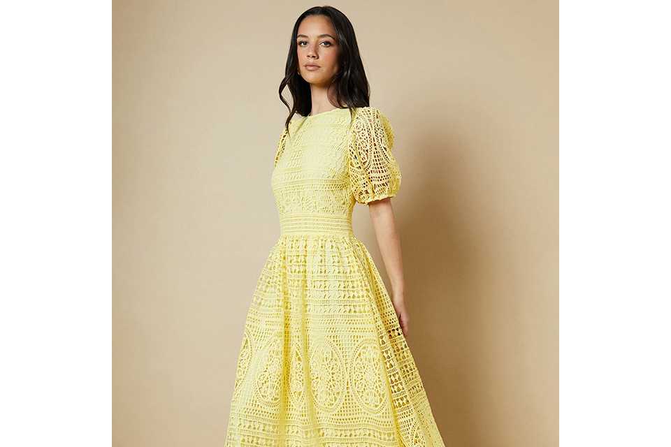 Black floral printed occasion dress with layered ruffle detailing, long sleeves and a high neckline, styled against a clean studio background.