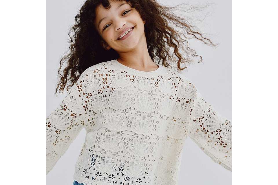 A young girl wearing a white crochet top and blue jeans.