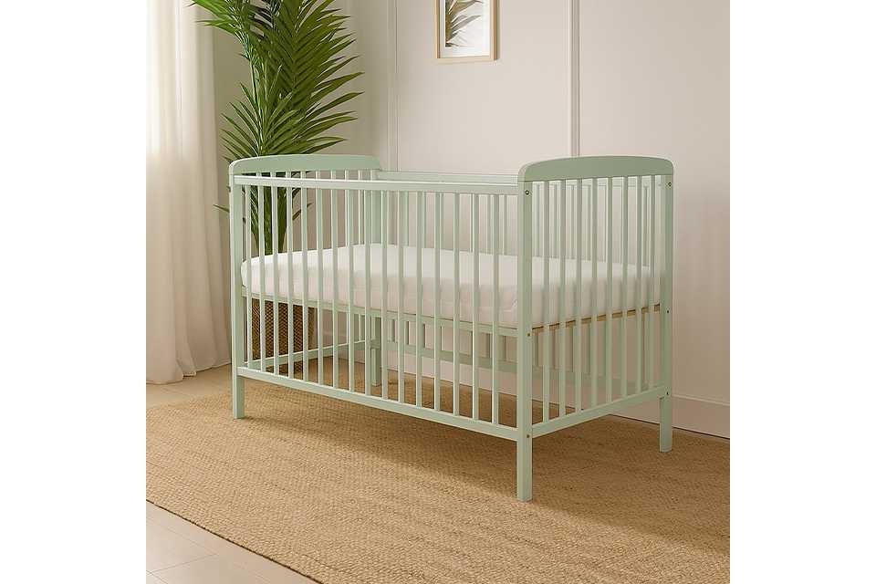 Pale green baby cot with mattress and plant in the background.