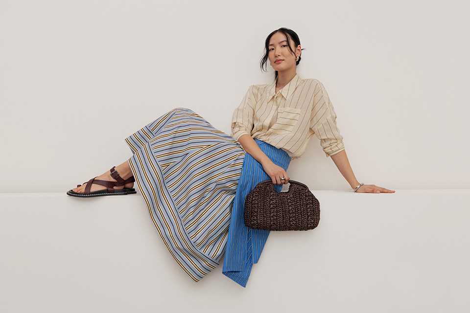 Woman wearing neutral striped top, witg a blueand yellow striped skirtand brown flat sandals.