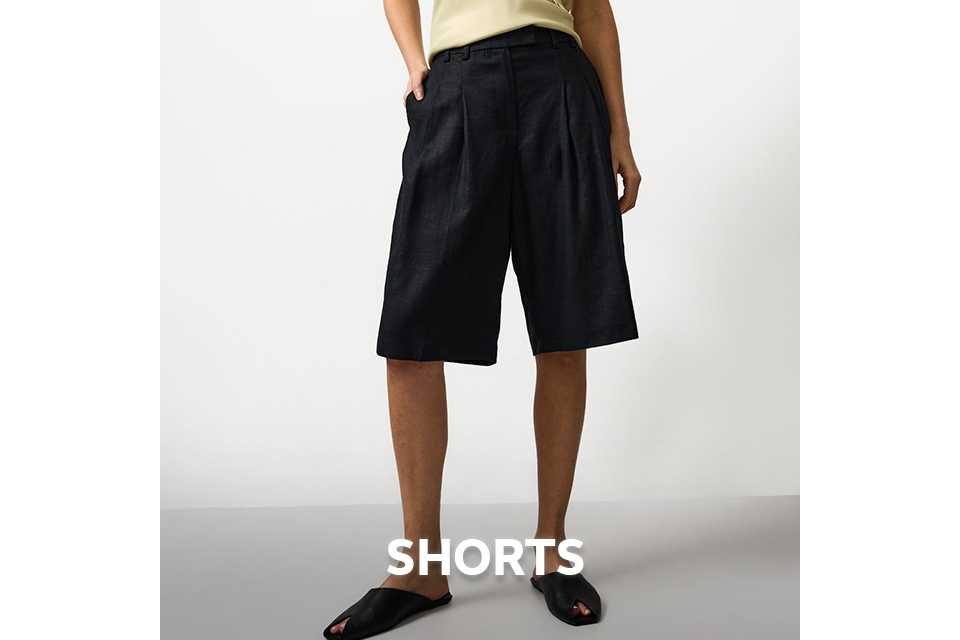 Woman wearing long black shorts with a butter yellow cami top.