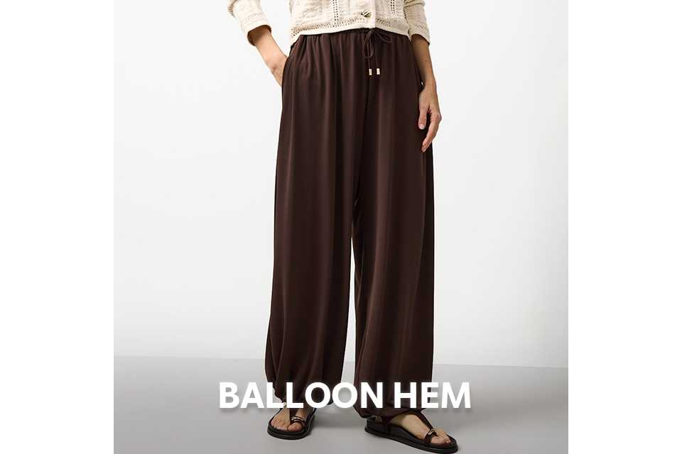 Woman wearing brown balloon trousers and cream neutral cardigan.
