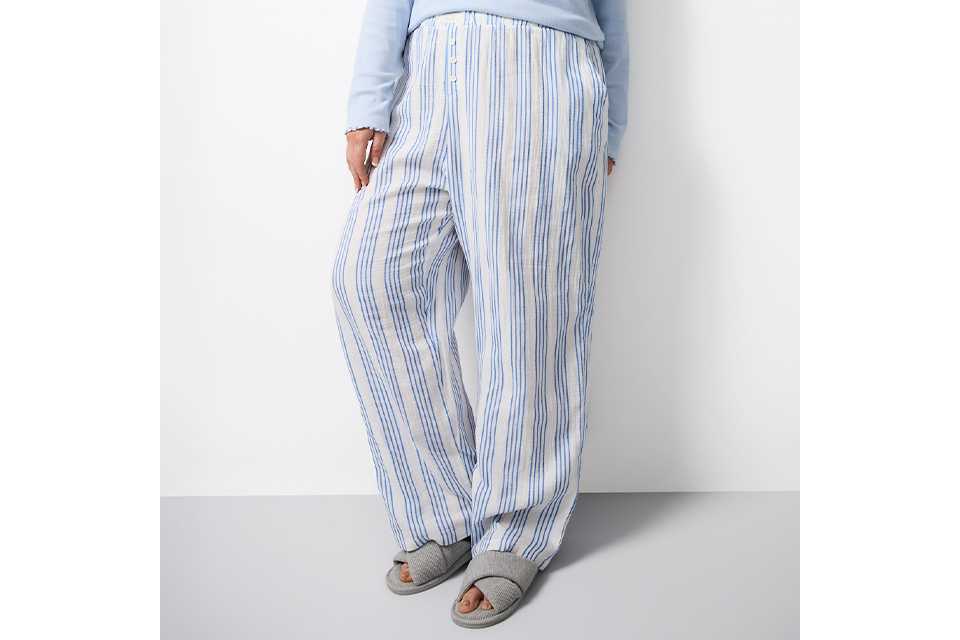 Women’s pastel green and white striped button‑up pyjama set with scalloped detailing, shown in a relaxed seated pose.