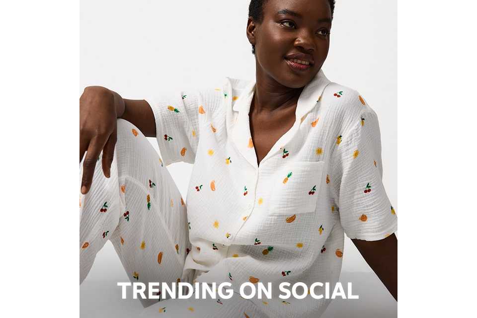 Person wearing a pink and red satin pajama set with a diamond pattern and decorative motifs, paired with beige slippers, standing against a plain white background.