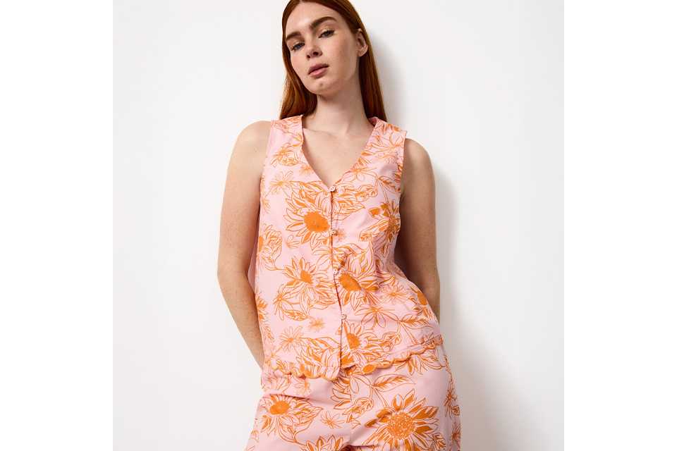 Women’s yellow floral satin pyjama top with purple and green botanical print, shown in a relaxed seated pose.