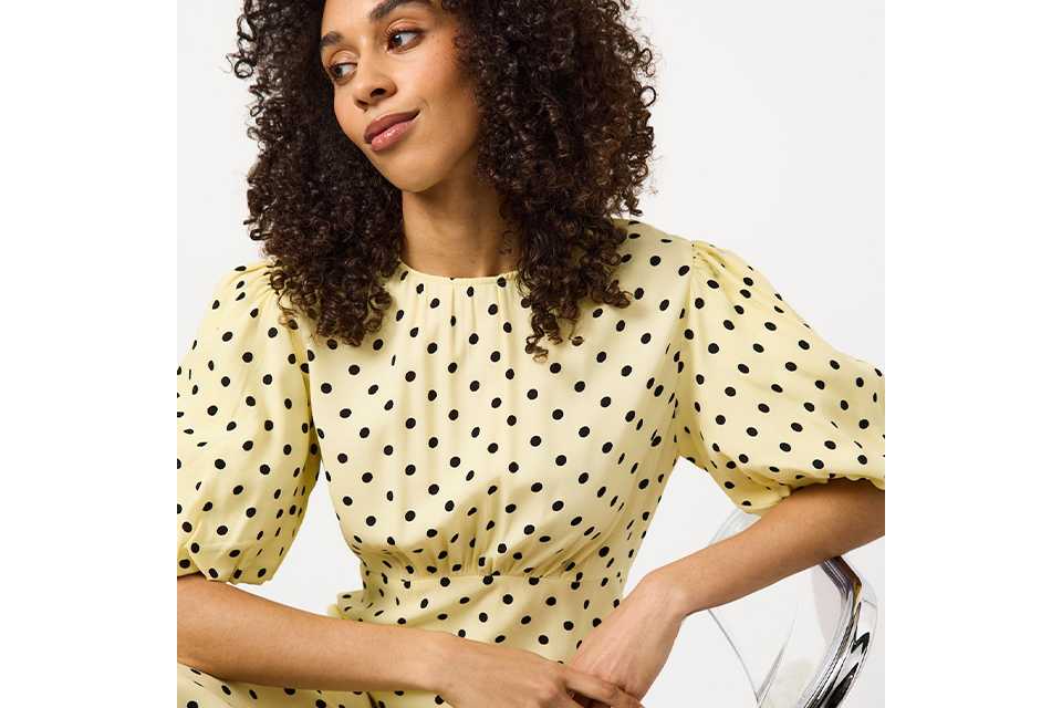 Person wearing a beige ribbed knit sweater paired with a dark skirt, standing against a plain white background.