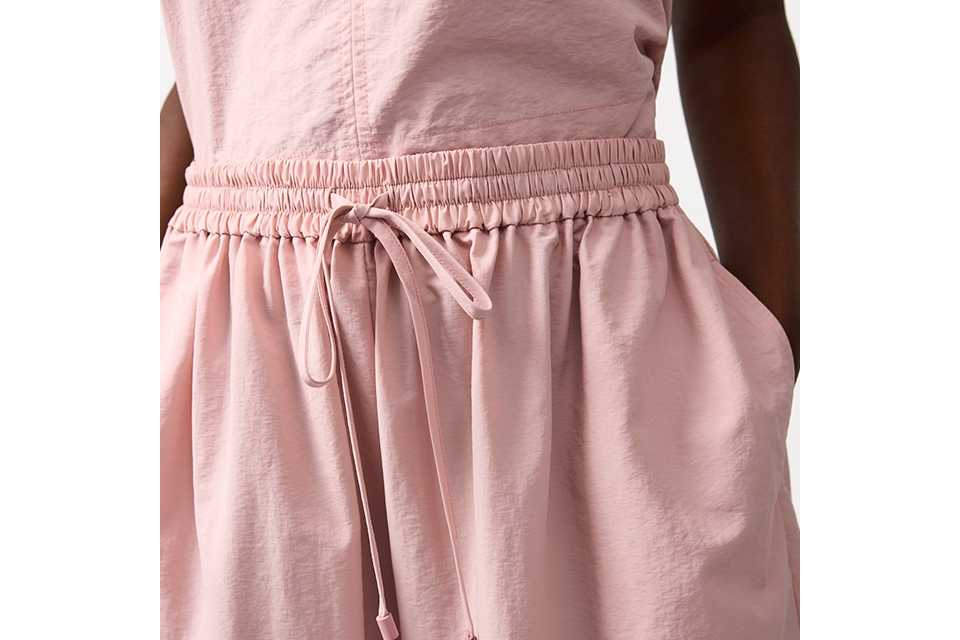 Cream sleeveless top and matching skirt styled with a black cut‑out bucket bag and crossbody strap on a neutral studio background.