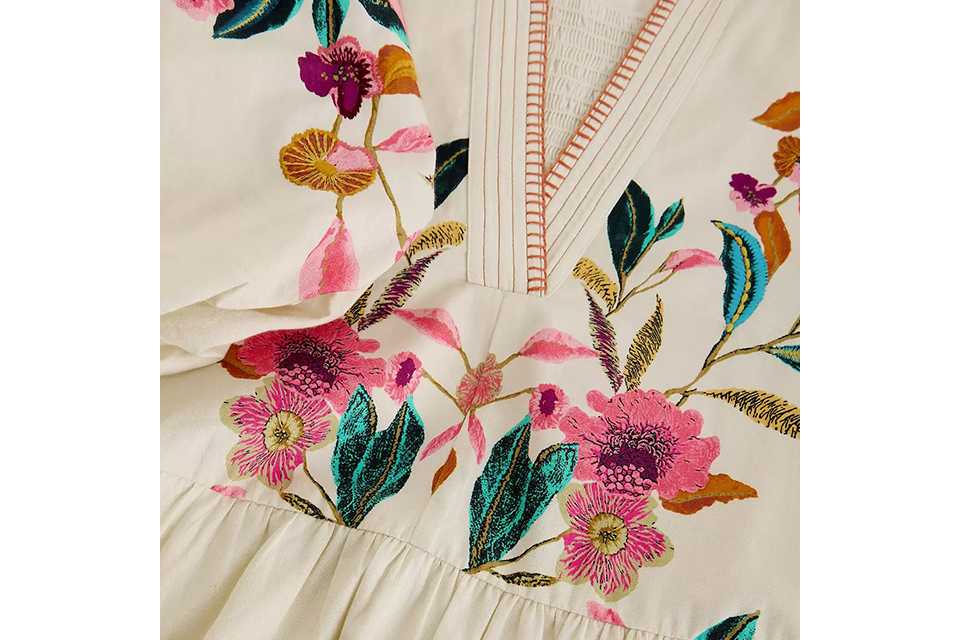 Pink floral tiered midi dress with short flutter sleeves and V‑neckline, styled with neutral heeled sandals on a light studio background.