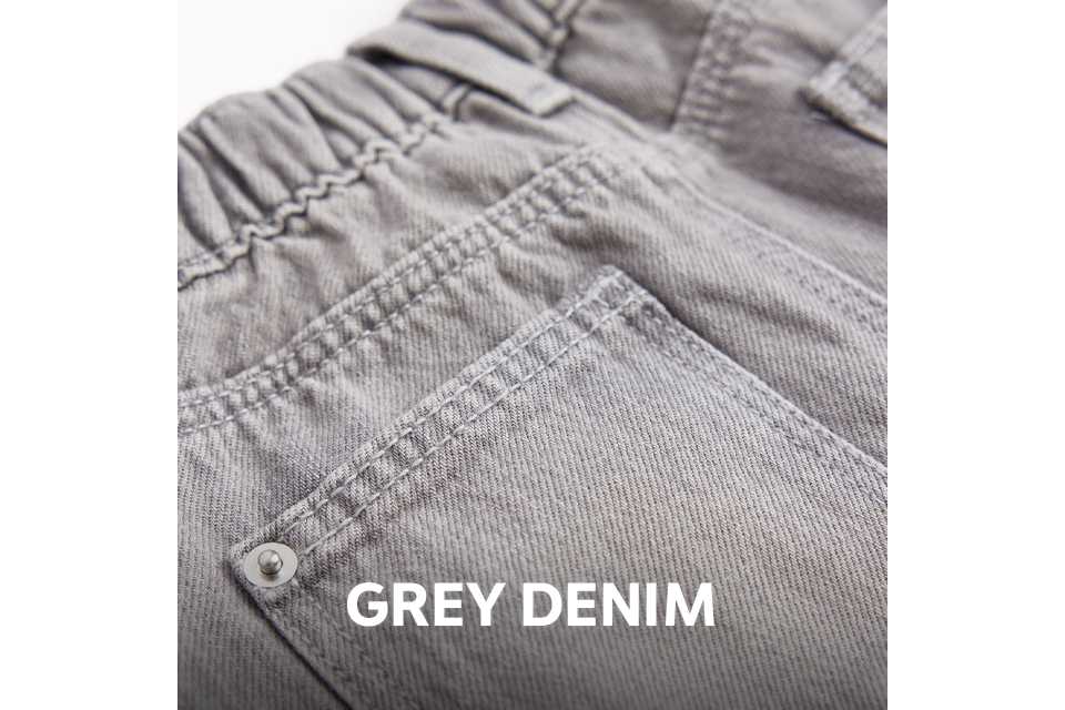 Close-up of the back of light grey denim jeans featuring an elasticated waistband, belt loops, and a back pocket with rivet detailing.