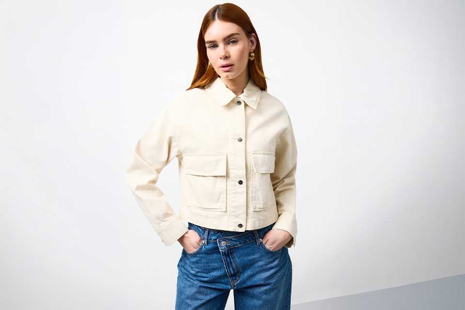 Cream cropped jacket layered over yellow shirt with blue jeans styled for UK staycation outfit.