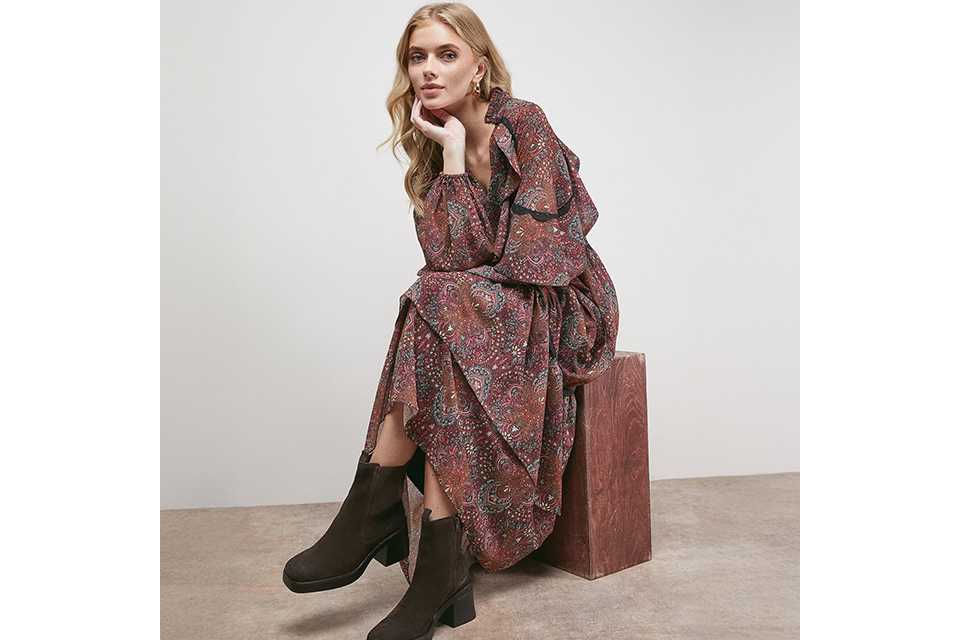 Woman wearing a floaty paisley dress, paired with brown boots.