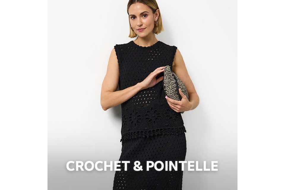 Woman wearing black crochet co ord, carrying a woven bag and wearing black flat sandals.