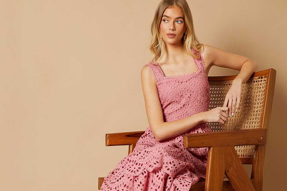 A woman sitting in a chair wearing a pink dress and brown block shoes.