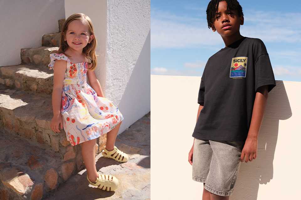 A picture showing two children, one child wearing a dress with graphic dress and yellow sandals, and the other wearing a black top with denim shorts.