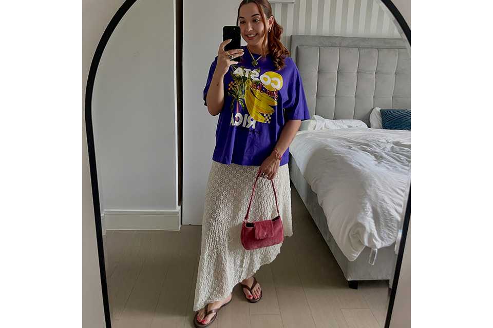 Wearing wearing a purple graphic top, with a white maxi long length skirt.
