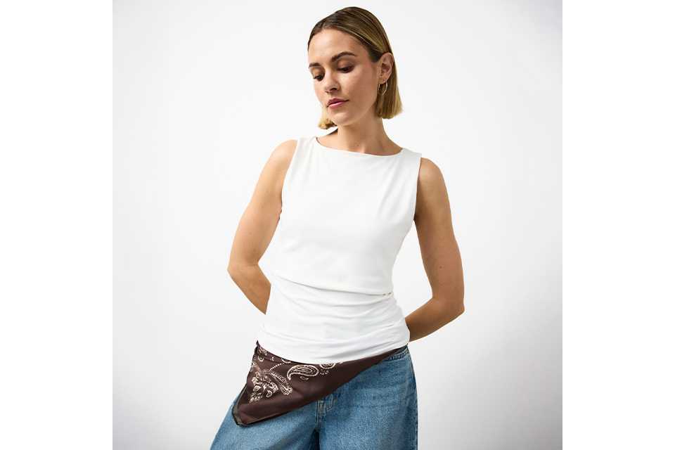 Woman wearing jeans and a white vest top.