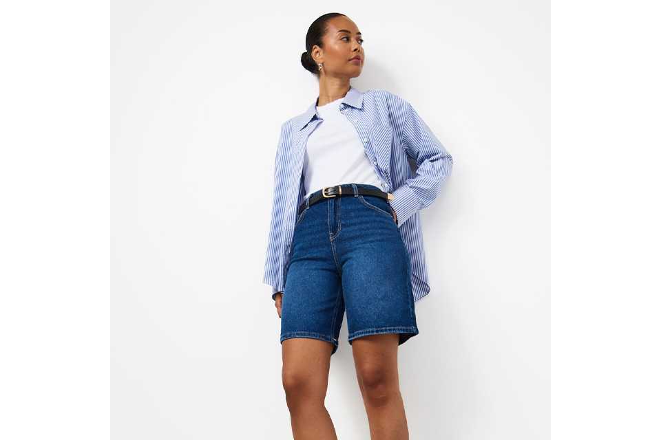 Woman wearing blue jorts, with a white basic tee, and a blue stripe shirt.