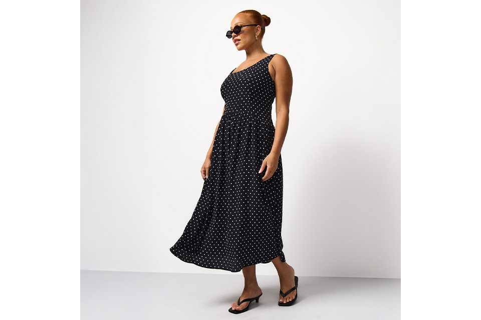 Black sleeveless midi dress with an all-over white polka dot print, featuring a fitted bodice and flowing skirt.