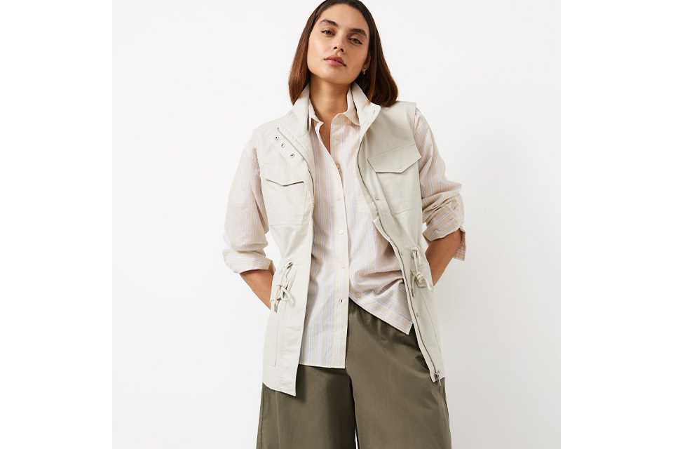 A woman wearing khaki balloon trousersm with a white shirt, and a neutral waistcoat.