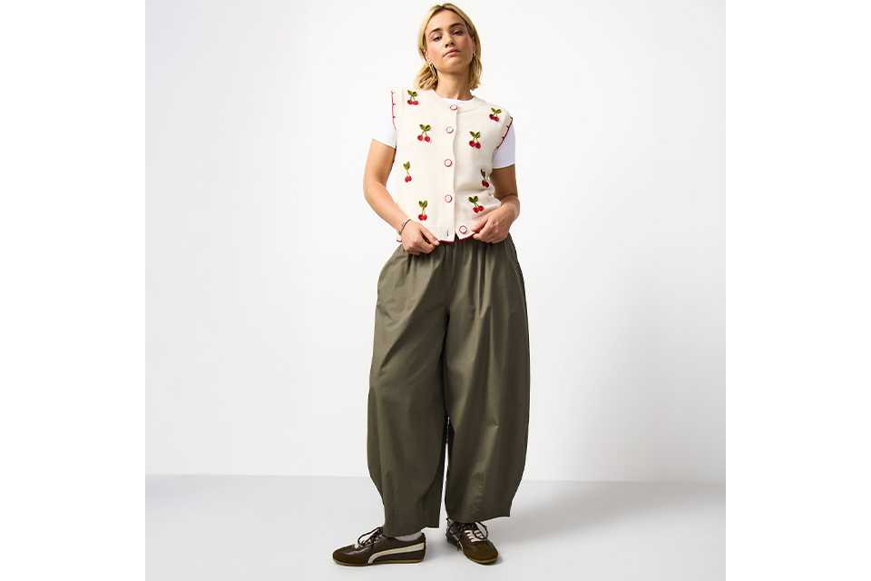 A woman wearing khaki balloon leg trousers, with a cherry print waistcoat.