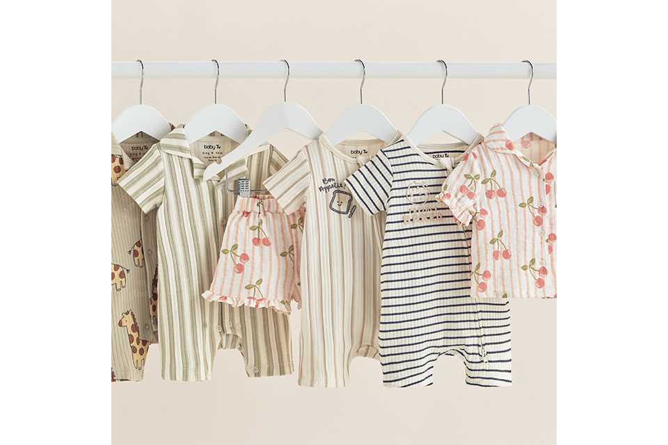 Baby clothing collection featuring striped rompers, animal print bodysuits, cherry print shorts and matching shirt sets hanging on a clothing rail.