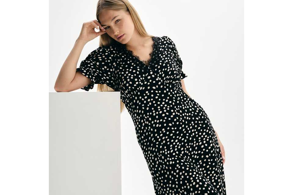 Black midi dress with white polka dot print and short ruffle sleeves, styled in a minimalist studio setting.
