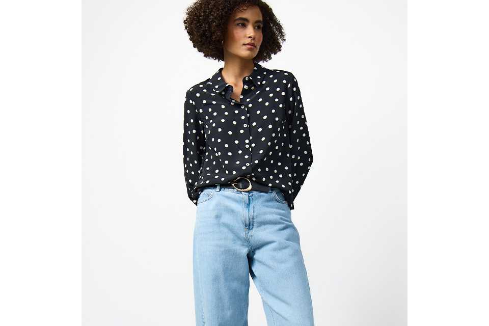 Navy blue polka dot button-through blouse styled with light wash wide-leg jeans and a black belt for a smart casual look.
