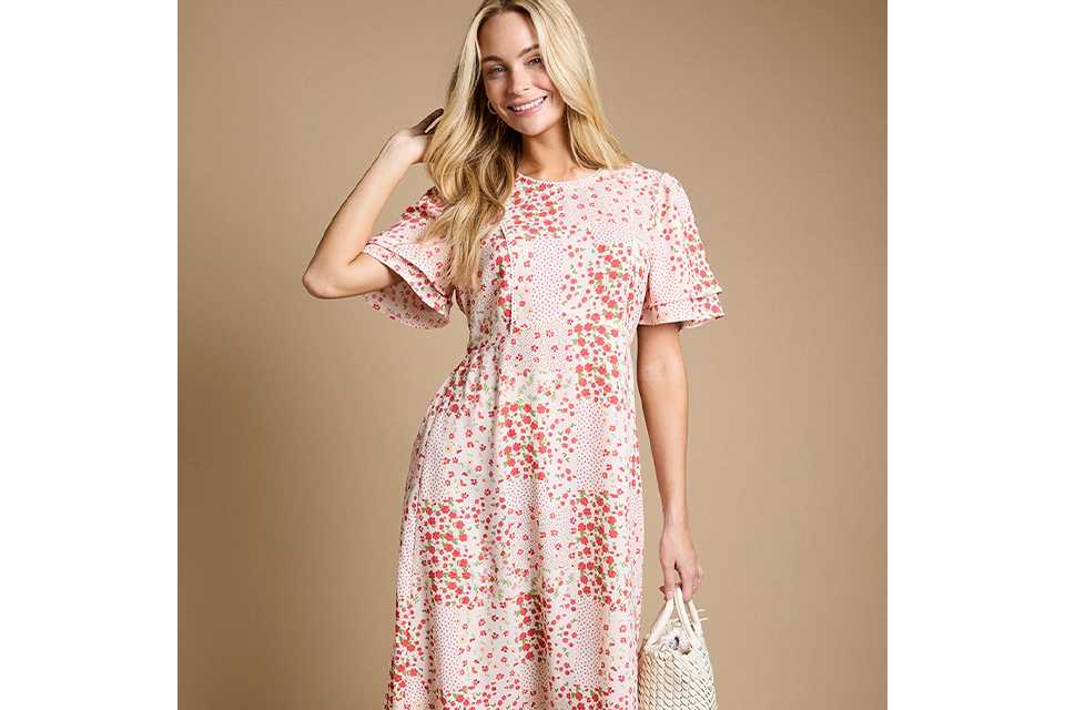 Blush pink floral print maxi dress with flutter sleeves, round neckline and flowing tiered silhouette, styled with a woven handbag.
