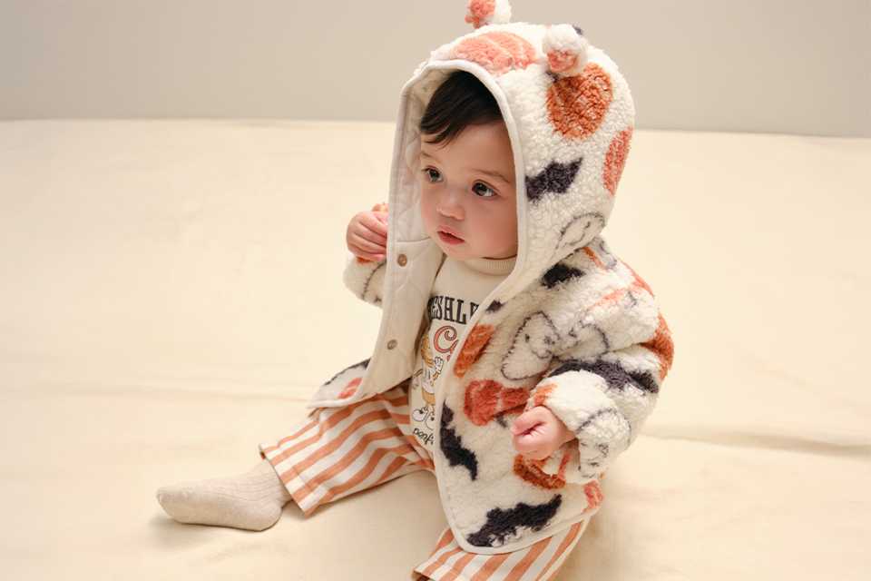 Baby Halloween outfit sets featuring pumpkin graphic sweatshirts, navy and cream harlequin trousers, and orange pumpkin-print leggings, displayed in a flat-lay clothing arrangement on a neutral background.