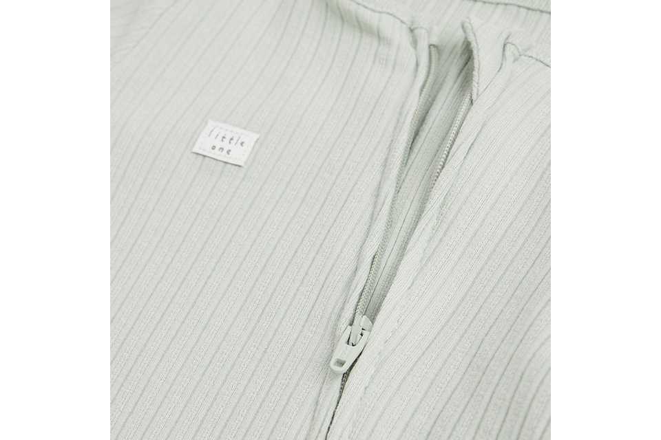 Close-up of a sage green ribbed baby sleepsuit with front zip fastening, crafted from soft stretch fabric for comfortable newborn and infant wear.