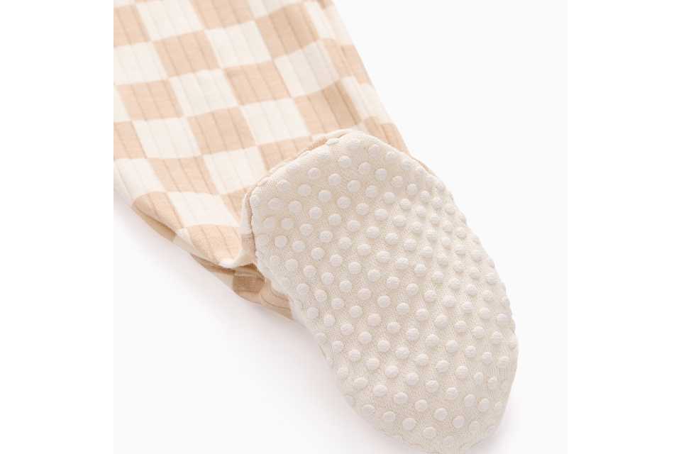 Close-up of a baby footed sleepsuit in a beige and cream check pattern, featuring an anti-slip sole with grip dots for added comfort and stability.