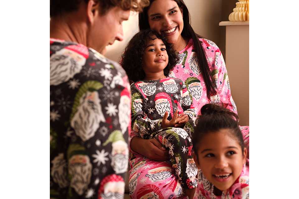 A family christmas mightwear image, with a family wearing matching pyjamas with santa on them, and a mix of a pink and black background.