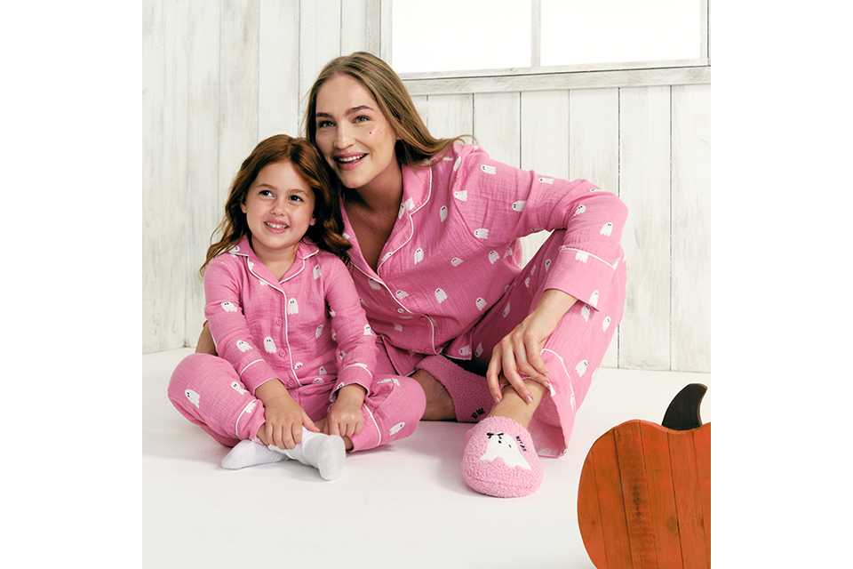 Person sitting on a bed wearing a cream graphic sweatshirt with a butter dish illustration and red gingham pyjama trousers, photographed in a cosy indoor setting.