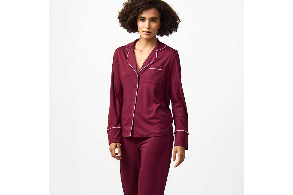 Women's satin pyjama set in burgundy with long-sleeve button-up top and matching trousers, comfortable coordinated nightwear.