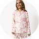 Child wearing a cream pyjama set with pink heart ribbon print, featuring a long-sleeve button-up sleep shirt and matching pajama trousers against a light studio background.