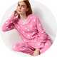 Person sitting in a white textured armchair wearing pink ghost-print pajama set with button-front shirt and matching lounge pants against a light studio background.