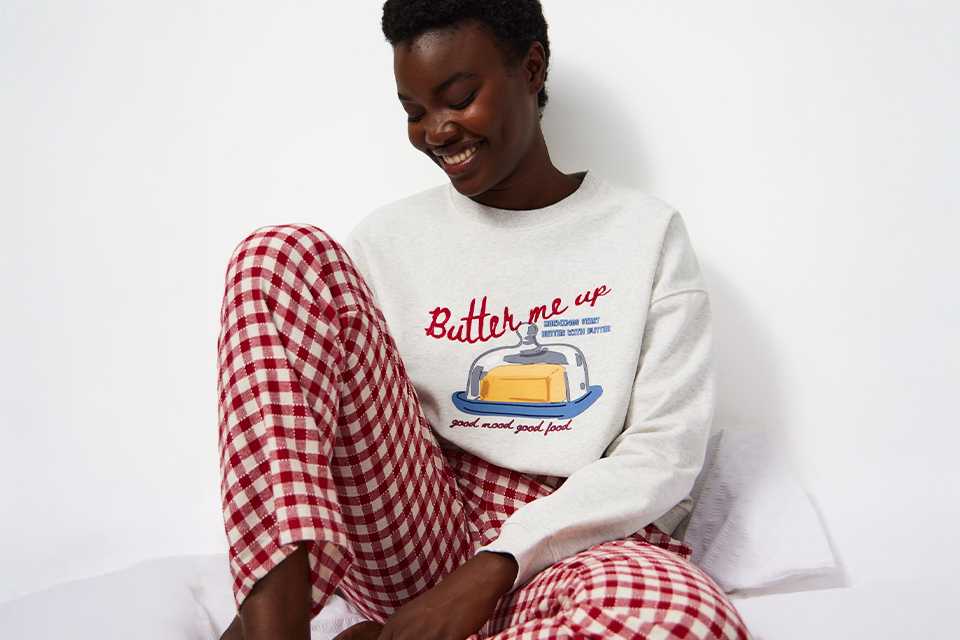 A woman wearing a pyjama set with red and cream gingham bottoms and a cream long sleeve pj top.