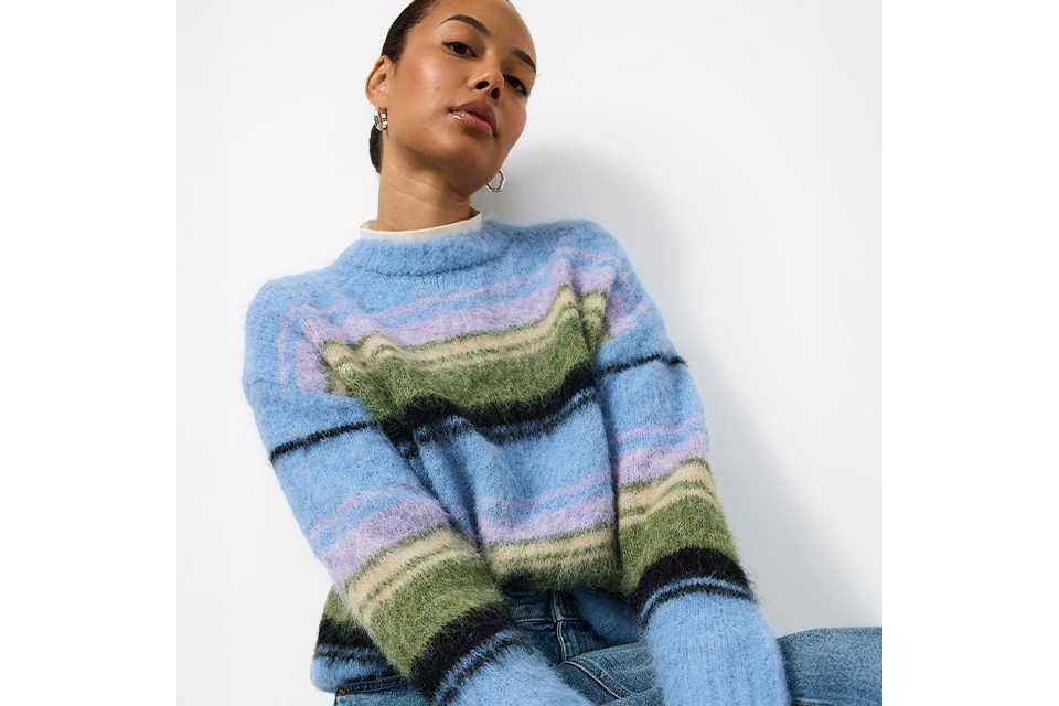 A woman wearing a knitted stripey jumper, with a light denim skirt.