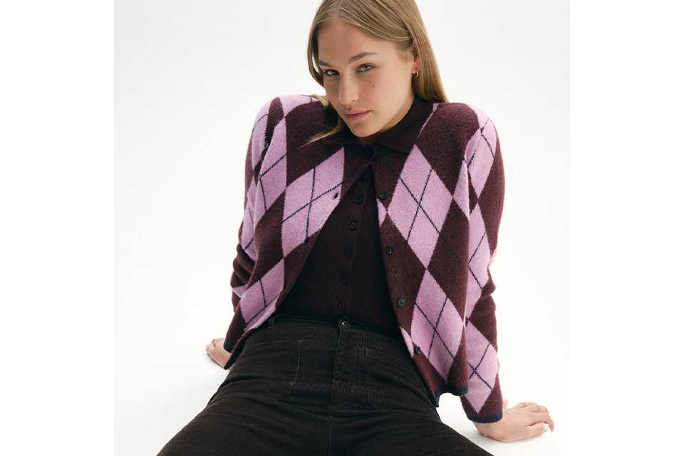 A woman wearing a black outfit with a purple argyle cardigan.