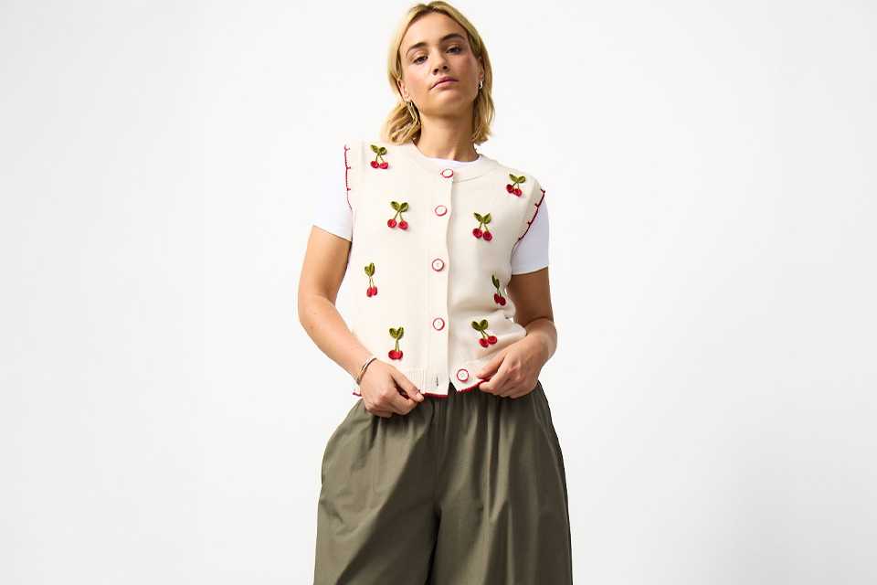 A woman wearing khaki balloon leg trousers, with a cherry print waistcoat.