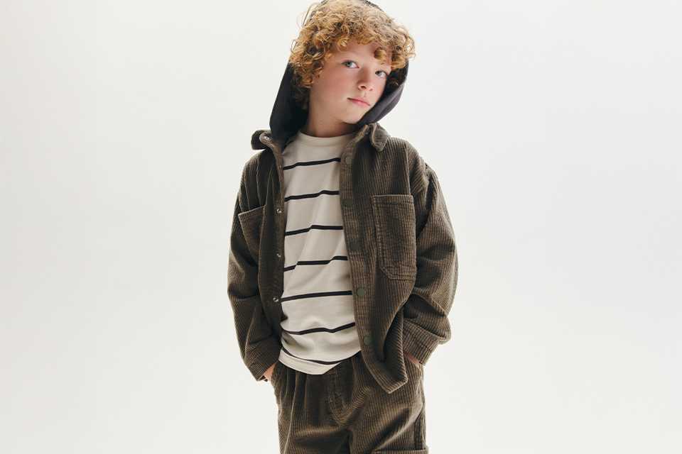 A boy wearing a corduroy co-ord, with a stripey top underneath.